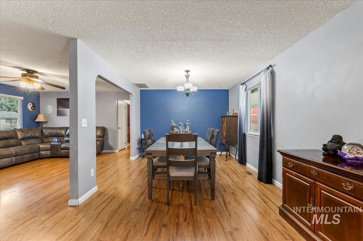 Dining room featuring light wood-type flooring, a chandelier, a textured ceiling, and a ceiling fan