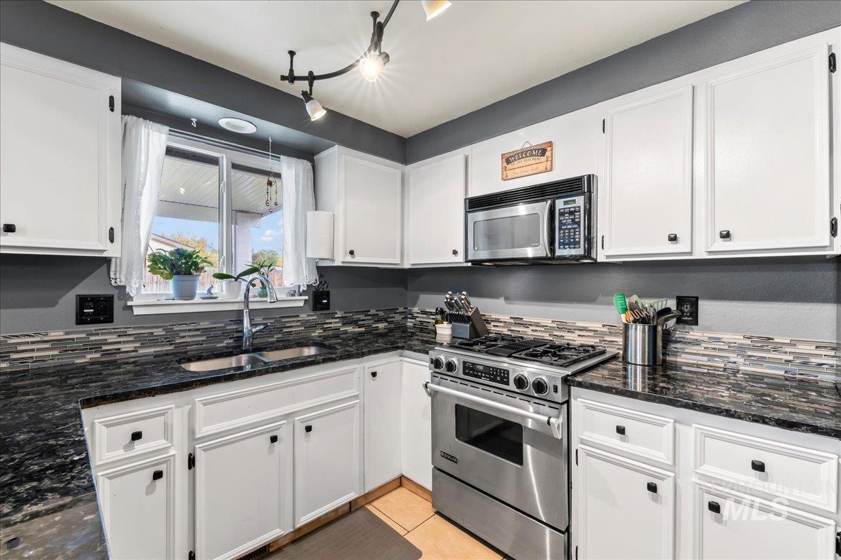 Kitchen with appliances with stainless steel finishes, white cabinetry, dark stone countertops, light tile patterned floors, and backsplash