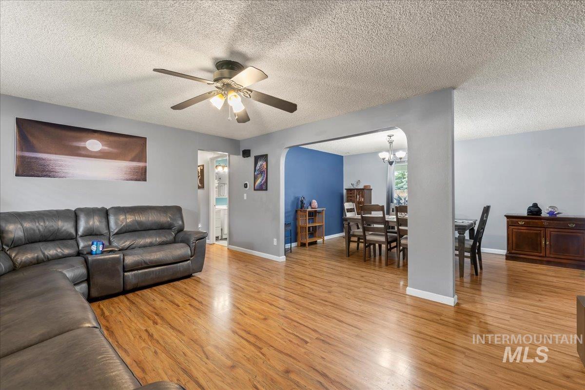 Living room with a textured ceiling, light wood-type flooring, ceiling fan, and a chandelier