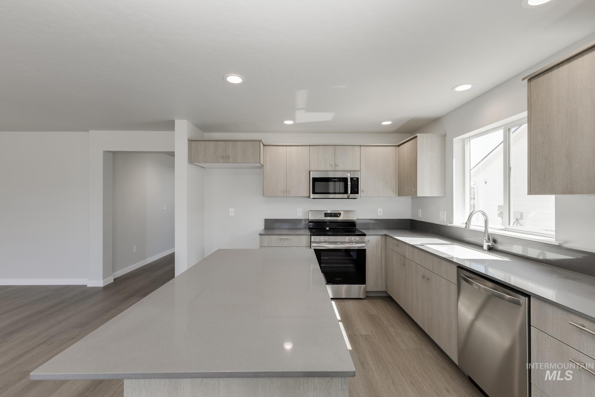Kitchen with stainless steel appliances, light brown cabinets, light wood-style floors, recessed lighting, and a kitchen island