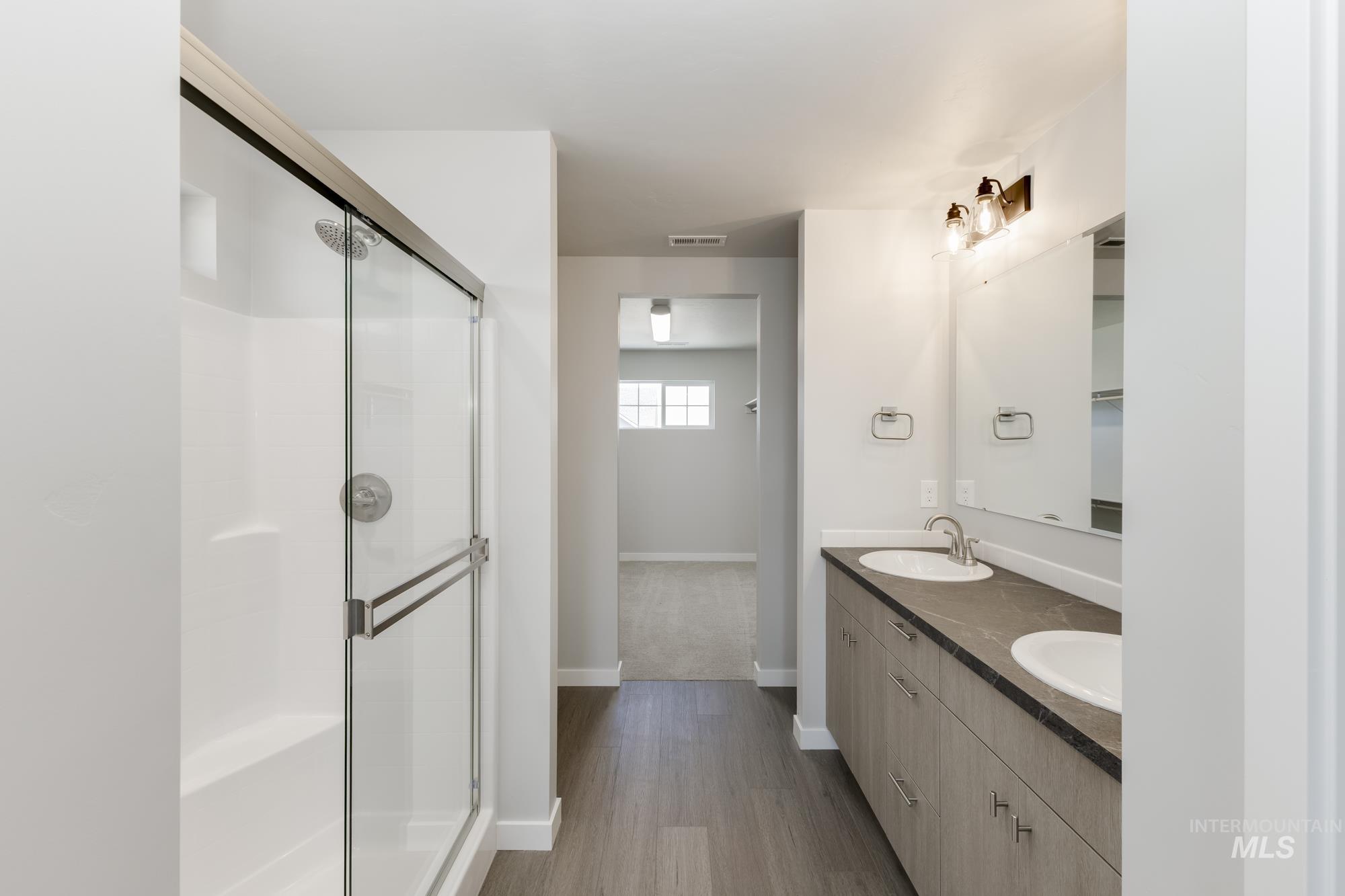 Full bath with double vanity, a shower stall, and wood finished floors
