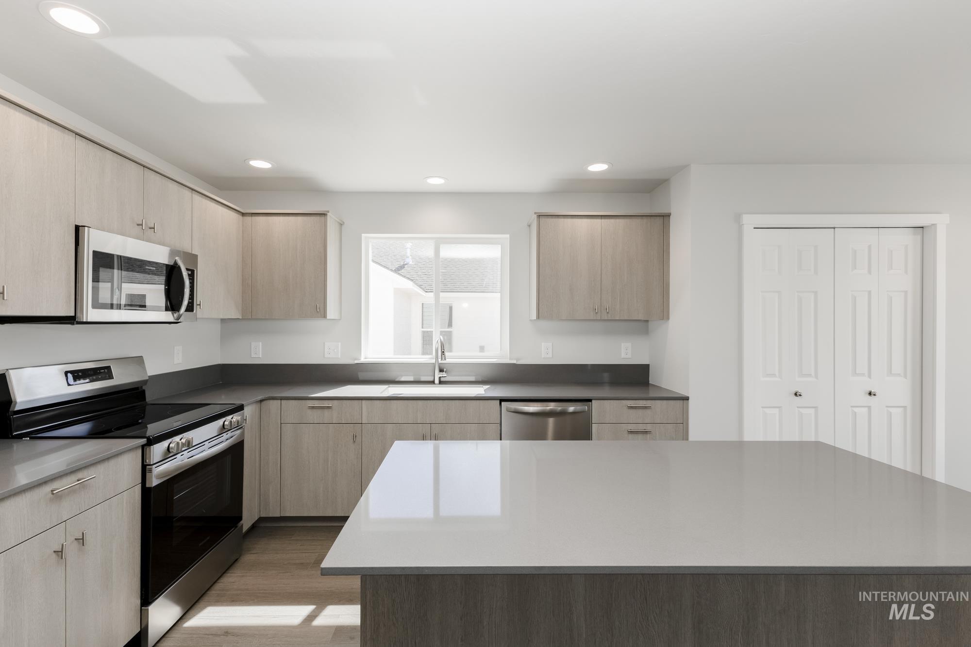Kitchen featuring stainless steel appliances, light brown cabinets, light wood-type flooring, recessed lighting, and a center island