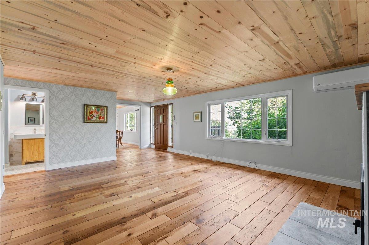Unfurnished living room featuring wallpapered walls, an accent wall, light wood finished floors, wood ceiling, and healthy amount of natural light