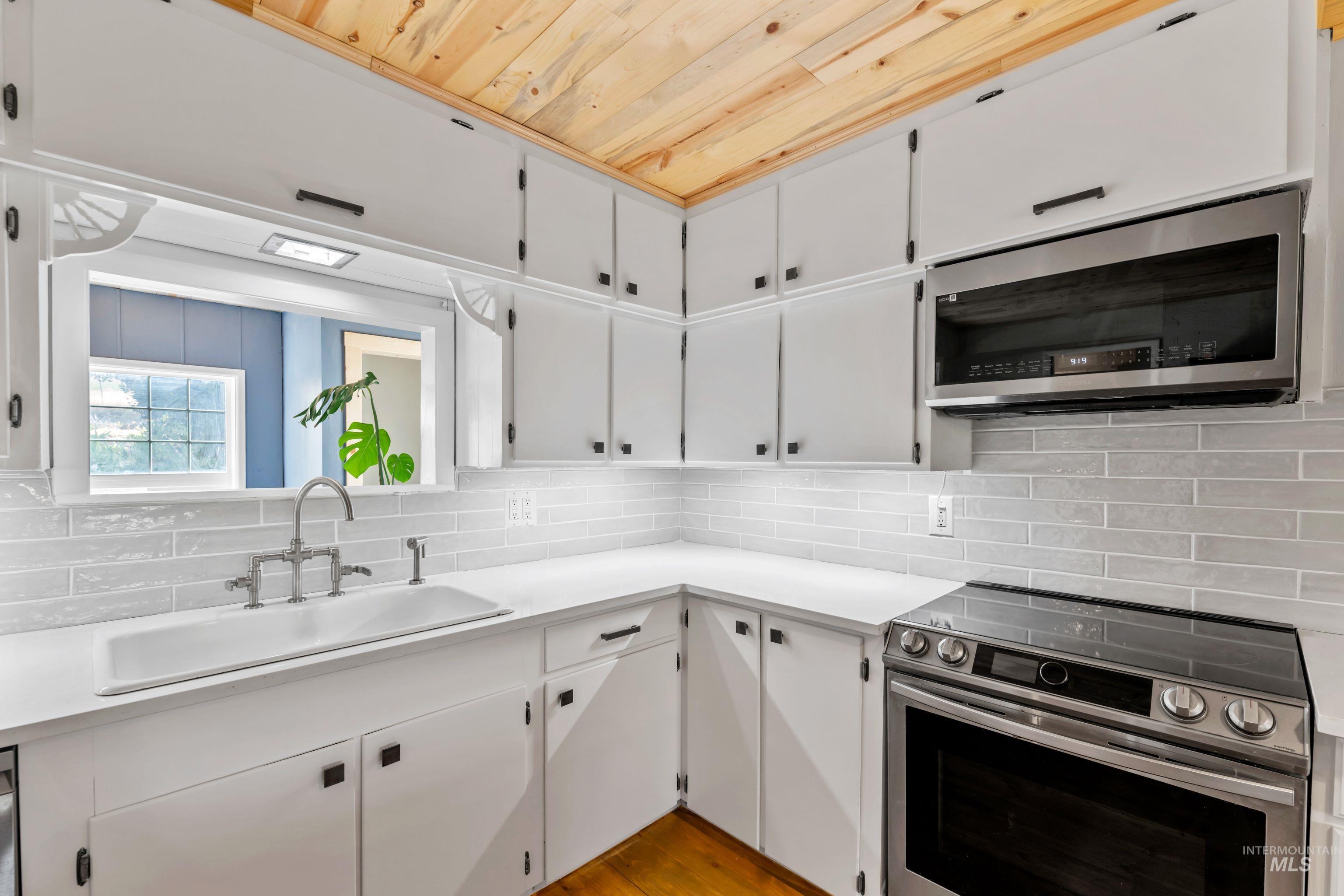 Kitchen featuring stainless steel appliances, wooden ceiling, hardwood floors, quartz countertops, and tile backsplash