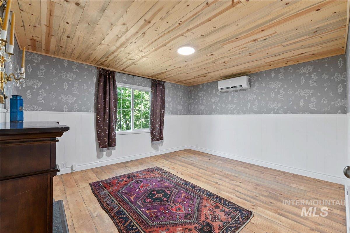Bedroom 3 featuring a wainscoted wall, wood ceiling, wallpapered walls, and hardwood flooring.  Fireplace is electric.