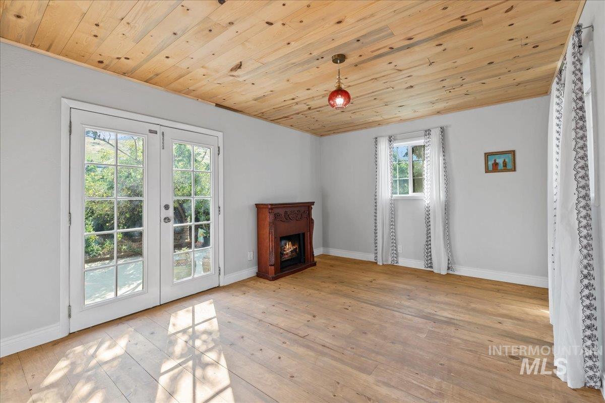 Master bedroom featuring french doors to outdoor patio, wood ceiling, hardwood floors, and a warm lit electric fireplace