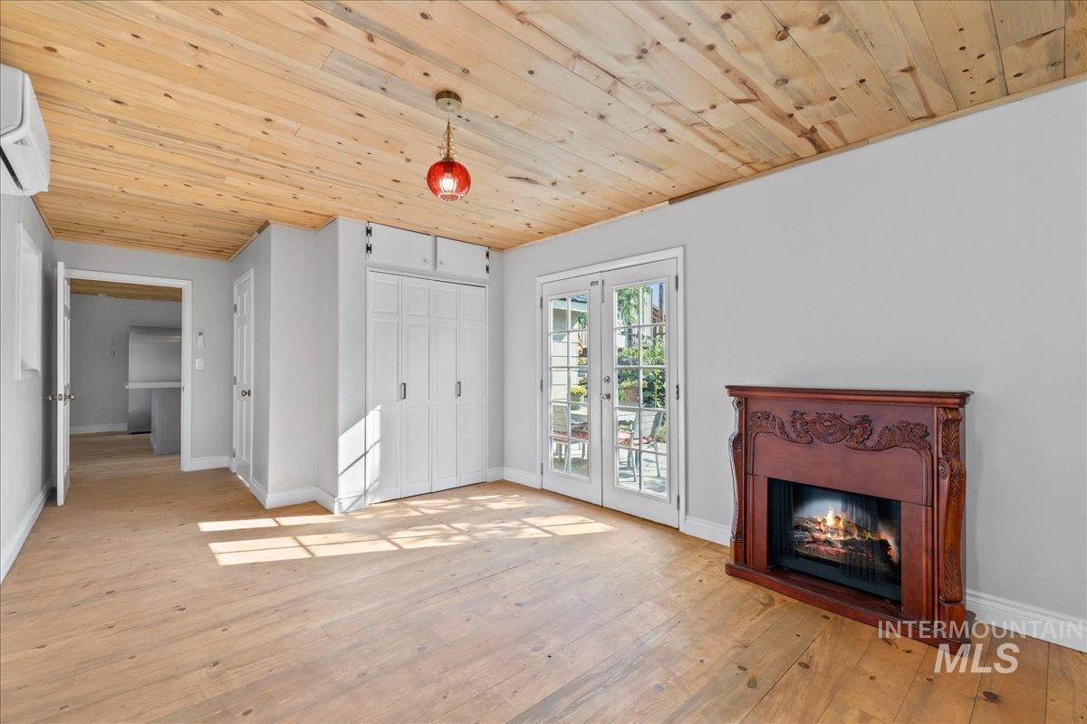 Master bedroom room with light wood-type flooring, wood ceiling, a glass covered fireplace, french doors to patio, and a wall heat/AC mini split and closet