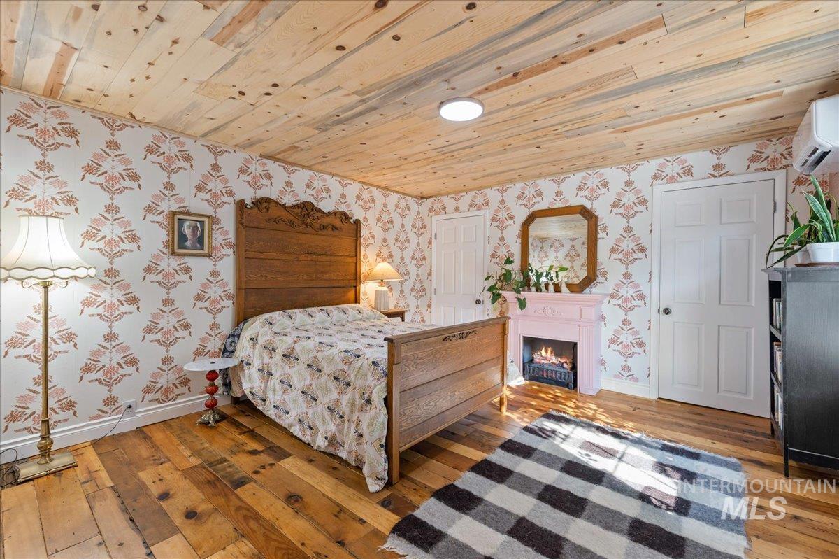 Bedroom 4 with wallpapered walls, light wood-style flooring, wooden ceiling, a warm lit fireplace, and a wall heat/AC mini split.  This bedroom is at the rear entrance of the home.  Most private bedroom.