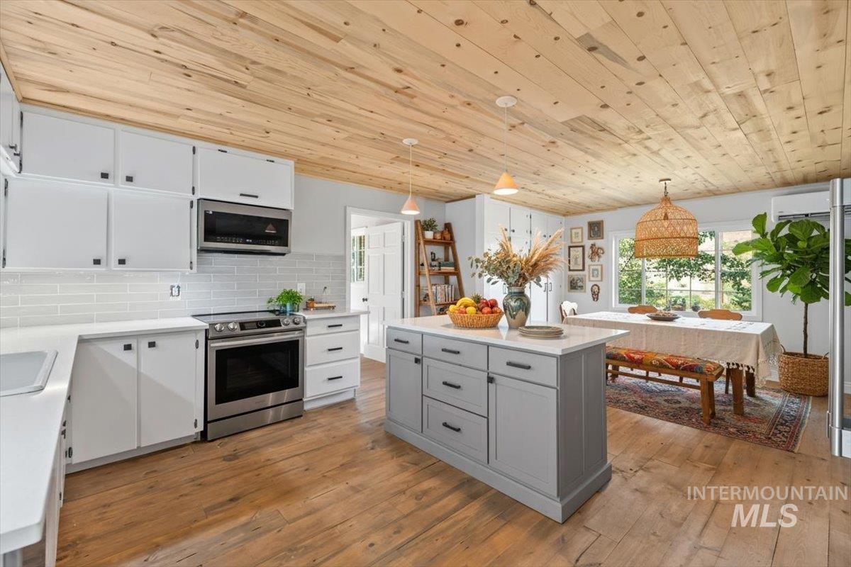 Kitchen featuring white cabinetry, decorative light fixtures, gray cabinets, appliances with stainless steel finishes, and wooden ceiling