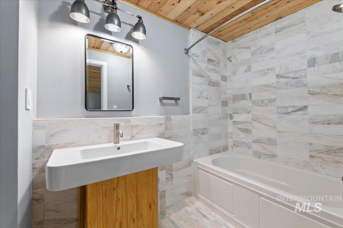 Bathroom with tile walls, shower / bathtub combination, wood ceiling, and wainscoting