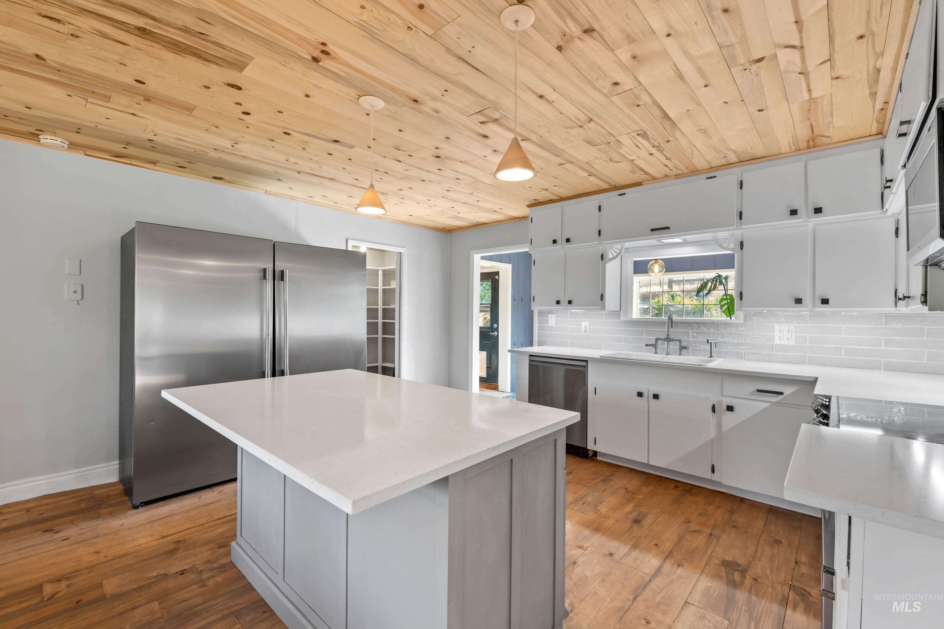 Kitchen featuring stainless steel appliances, wooden ceiling, hardwood floors, quartz countertops, and tile backsplash