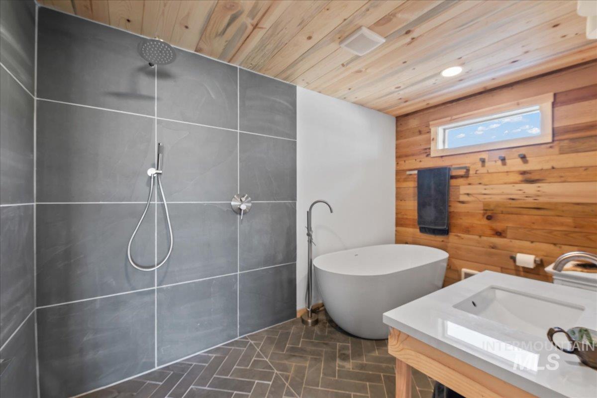 ADU spa like full bathroom with wood walls, wooden ceiling, tiled shower, vanity, toilet and a large soaking tub