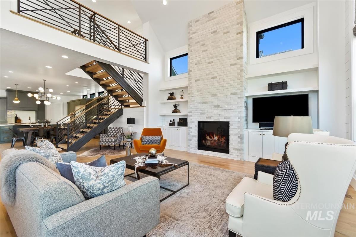 Living area with a towering ceiling, light wood-style floors, stairs, a tiled fireplace, and built in shelves