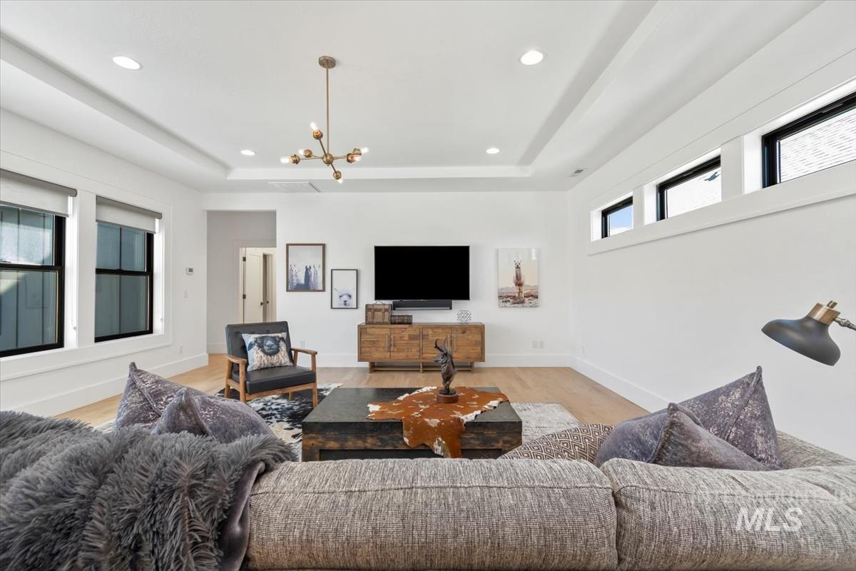 Living room with a raised ceiling, light wood-type flooring, recessed lighting, and a chandelier
