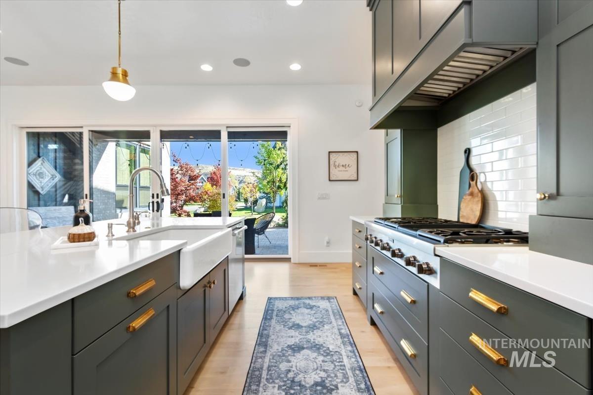 Kitchen featuring hanging light fixtures, light wood finished floors, recessed lighting, under cabinet range hood, and tasteful backsplash