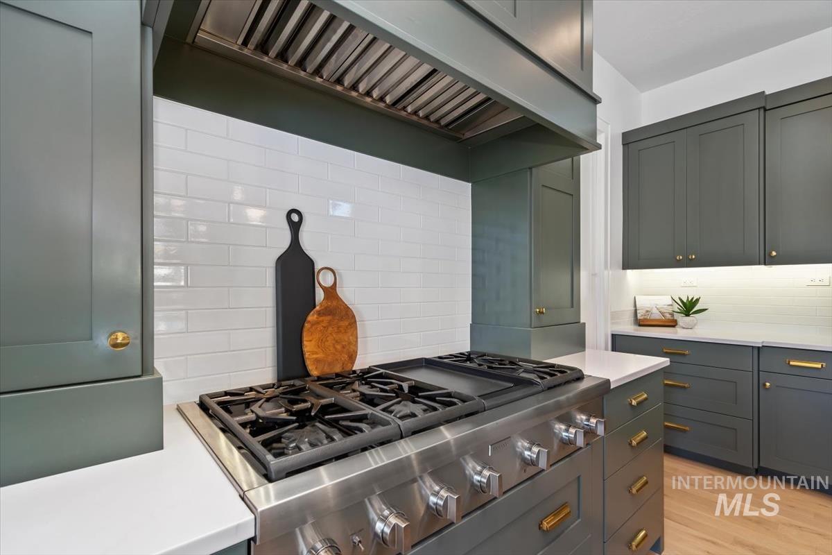 Kitchen featuring custom exhaust hood, stainless steel gas cooktop, tasteful backsplash, light wood-type flooring, and light stone counters