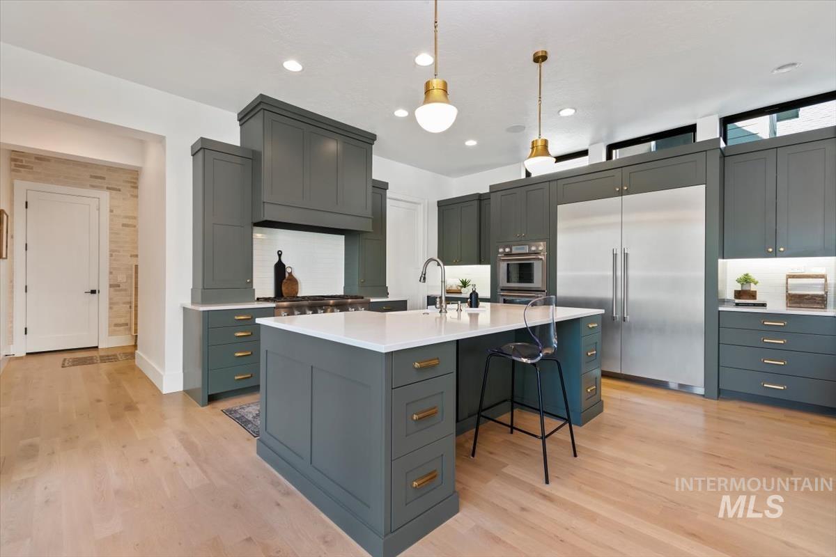 Kitchen with a breakfast bar area, pendant lighting, stainless steel appliances, a center island with sink, and light wood-type flooring