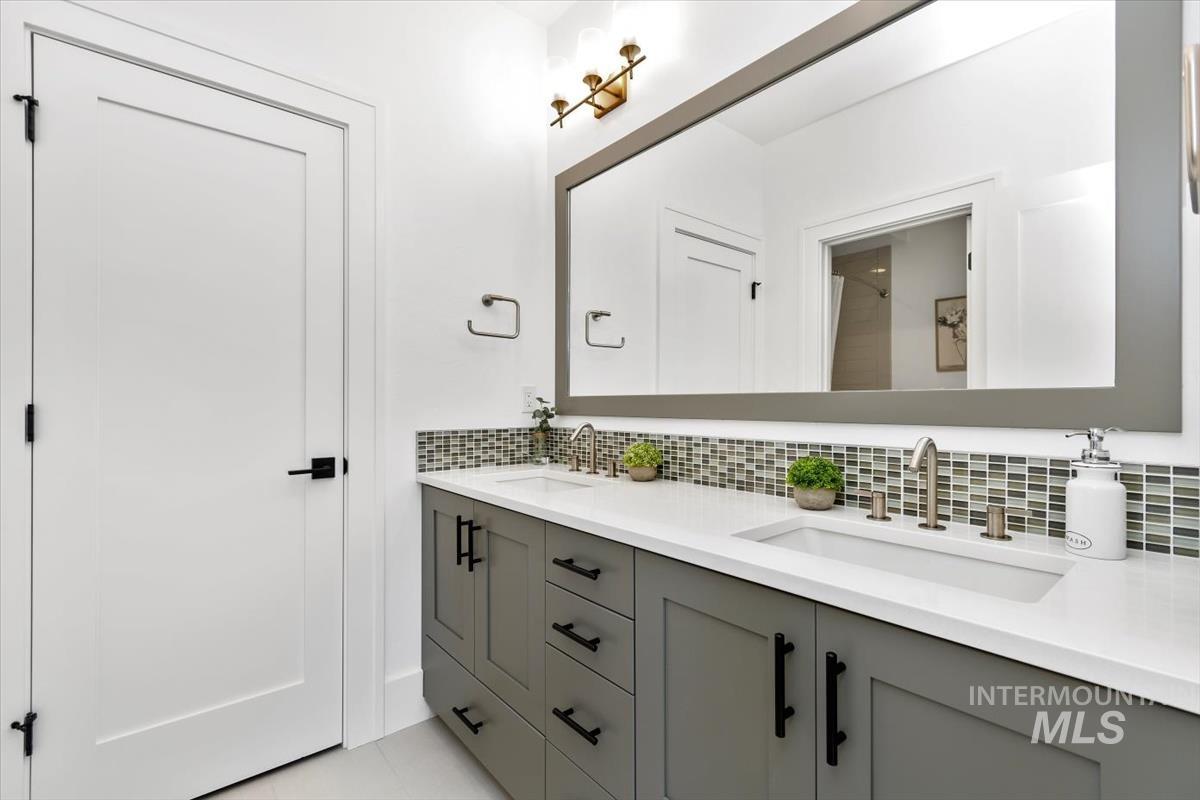 Full bath with tasteful backsplash, double vanity, a shower, and light tile patterned floors