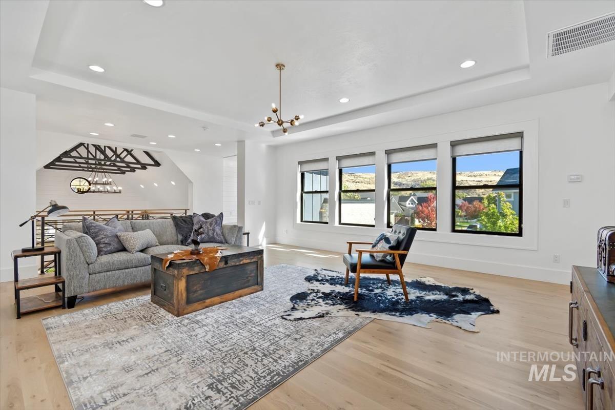 Living area with a raised ceiling, light wood finished floors, recessed lighting, and a chandelier
