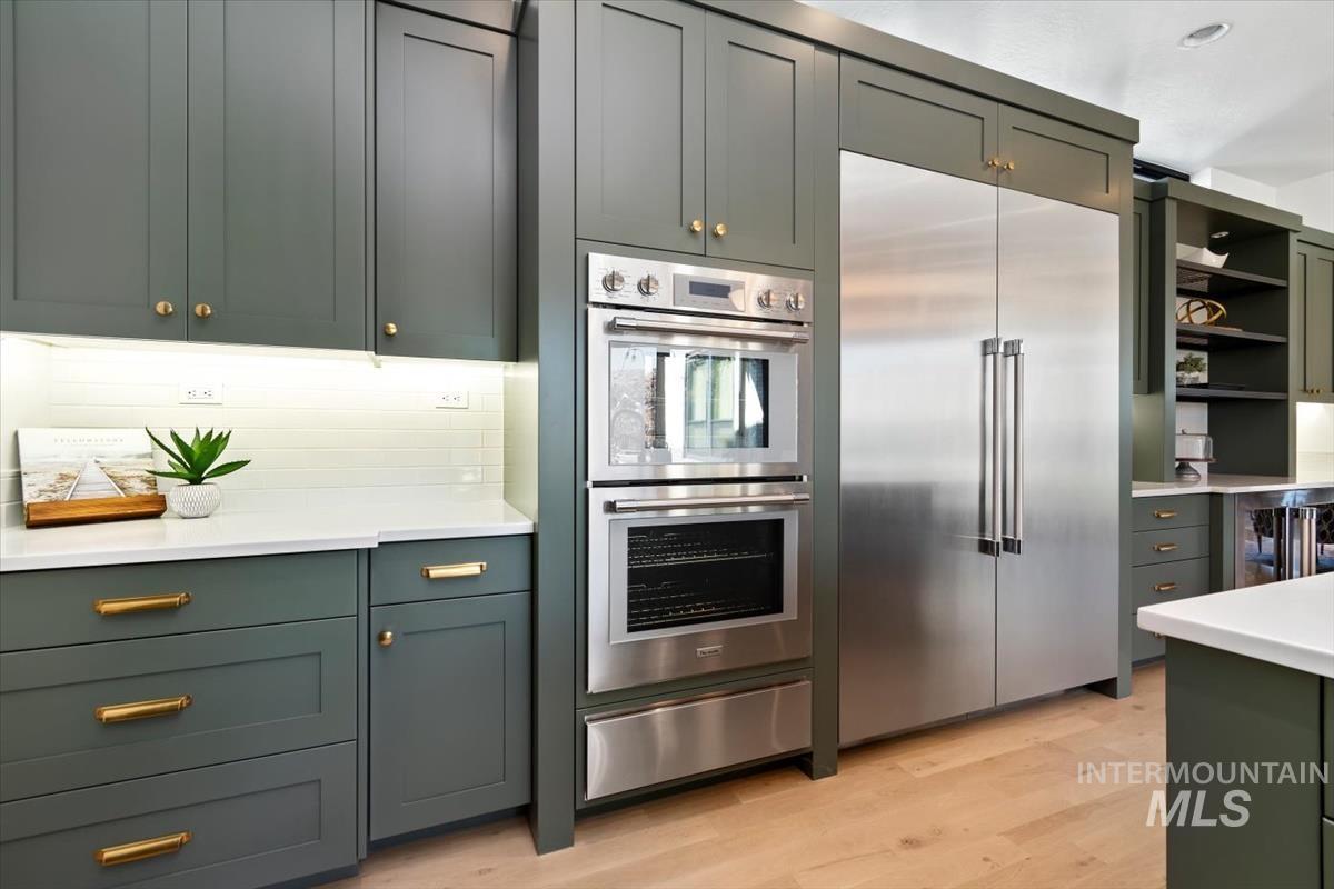 Kitchen featuring stainless steel appliances, open shelves, a warming drawer, light wood-type flooring, and green cabinetry