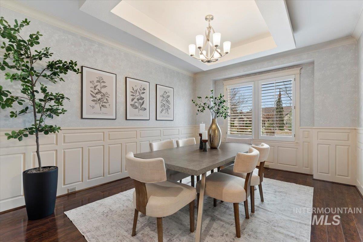 Dining room with a wainscoted wall, a decorative wall, dark wood-style floors, hanging lights, and ornamental molding