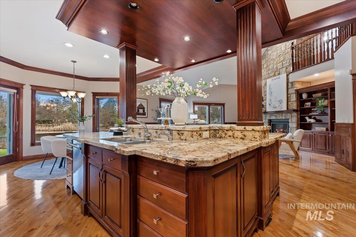 Kitchen with light stone counters, an island with sink, hanging lights, a stone fireplace, and built in features