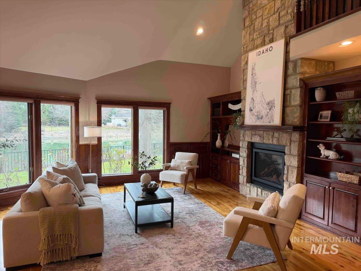 Living room with wainscoting, light wood-type flooring, a stone fireplace, vaulted ceiling, and recessed lighting