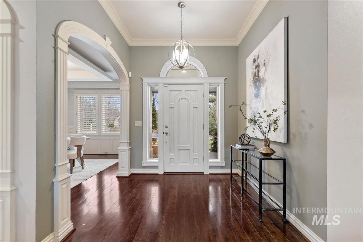 Entrance foyer featuring dark wood-style flooring, crown molding, and a chandelier