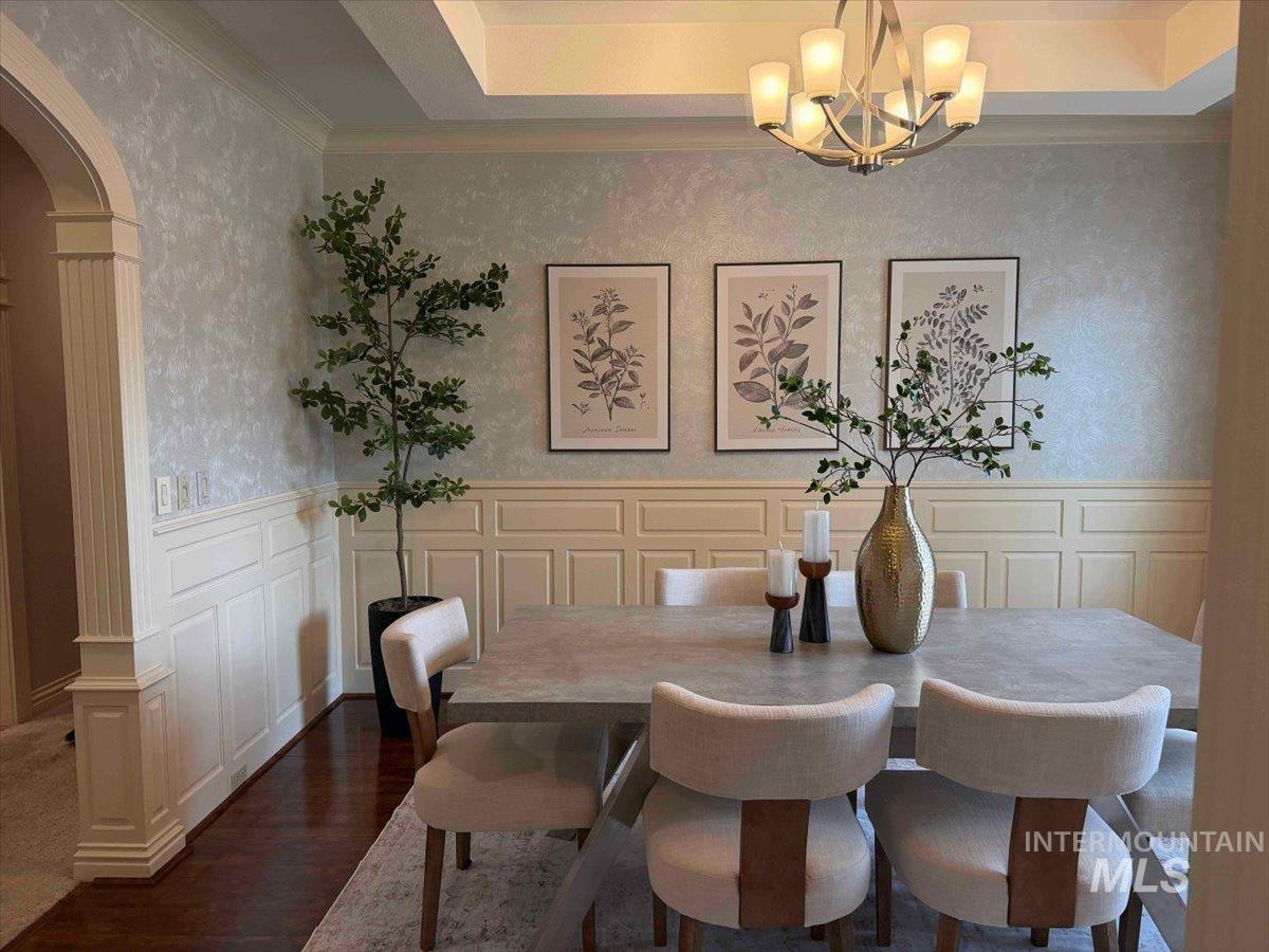 Dining room featuring a decorative wall, wainscoting, arched walkways, wallpapered walls, and dark wood-type flooring