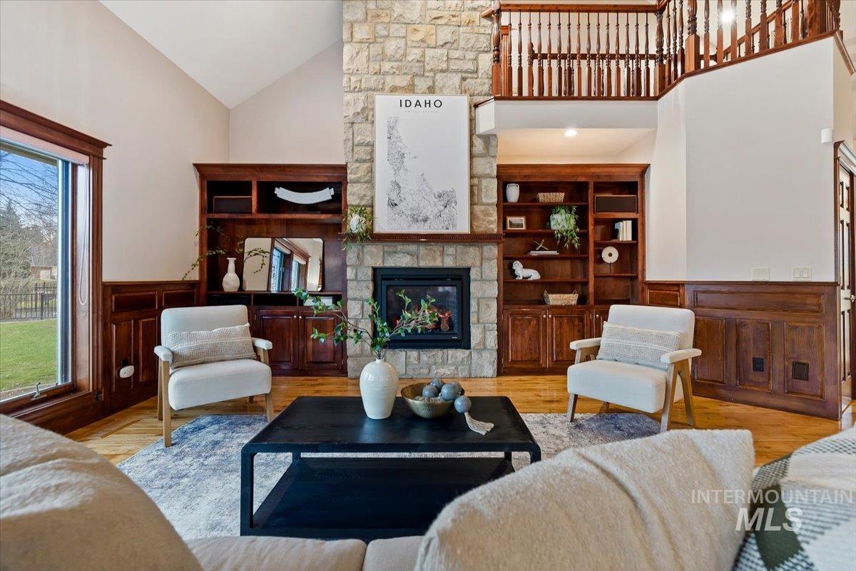 Living room with wainscoting, a decorative wall, a fireplace, light wood-style flooring, and vaulted ceiling