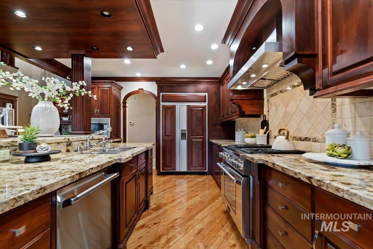 Kitchen with light stone counters, built in appliances, light wood-type flooring, arched walkways, and exhaust hood