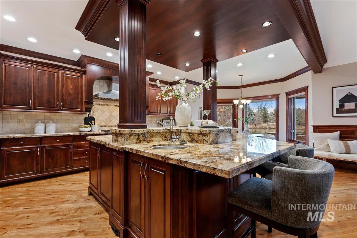 Kitchen with light stone countertops, light wood finished floors, ornamental molding, a spacious island, and a kitchen breakfast bar