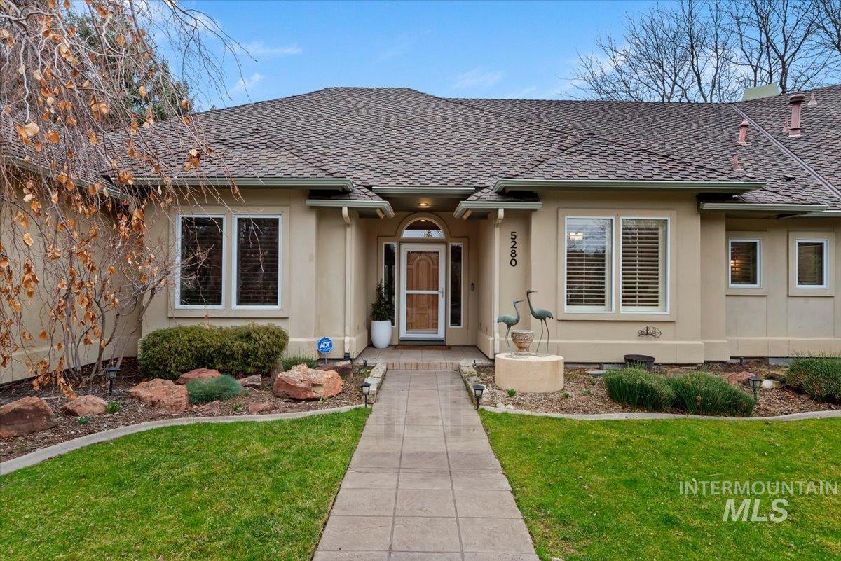 Doorway to property featuring roof with shingles, a yard, and stucco siding