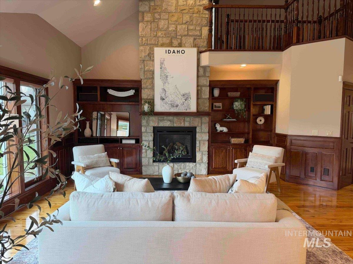 Living room with a stone fireplace, wood finished floors, vaulted ceiling, wainscoting, and recessed lighting