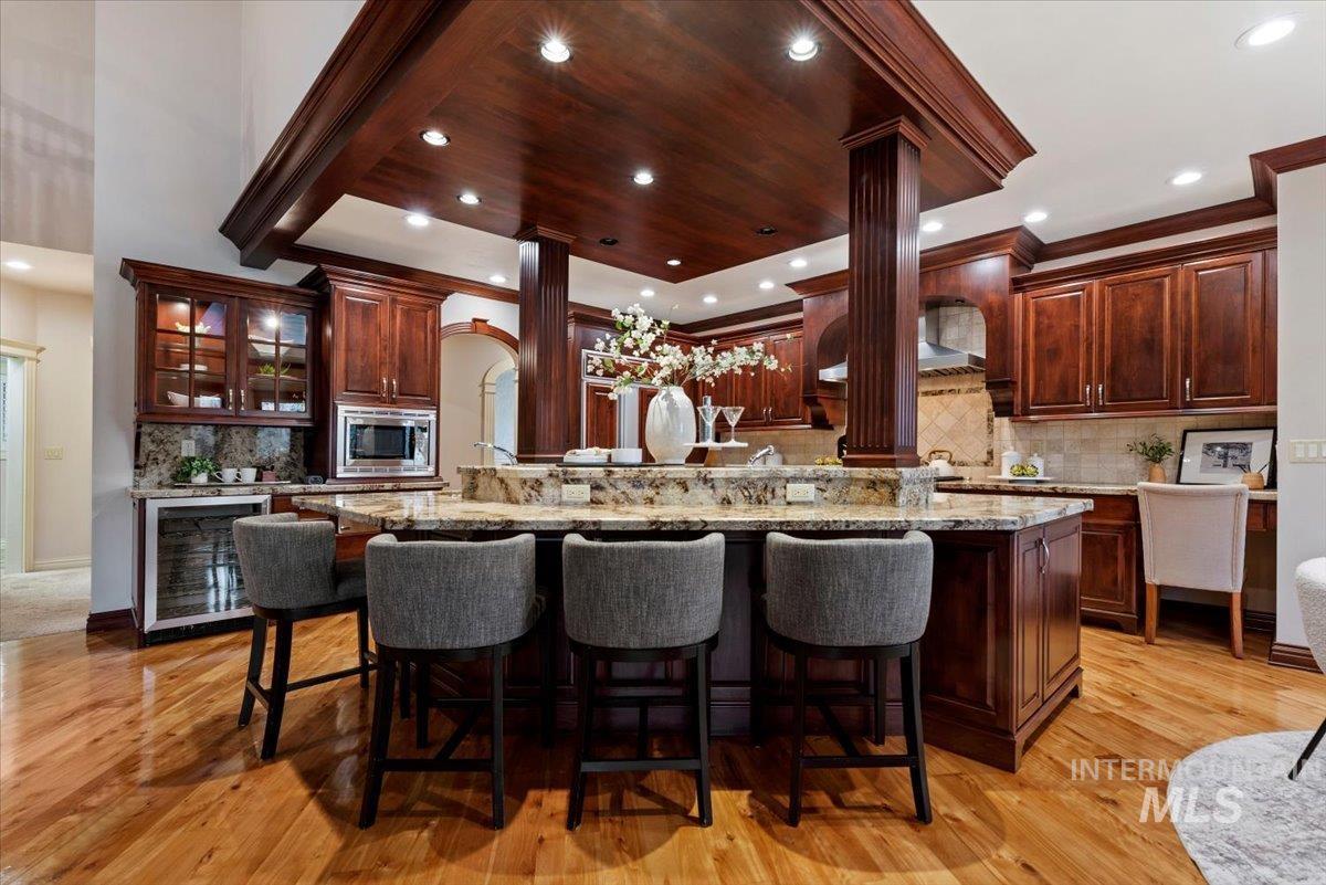 Kitchen featuring light stone countertops, decorative backsplash, wine cooler, a kitchen breakfast bar, and recessed lighting