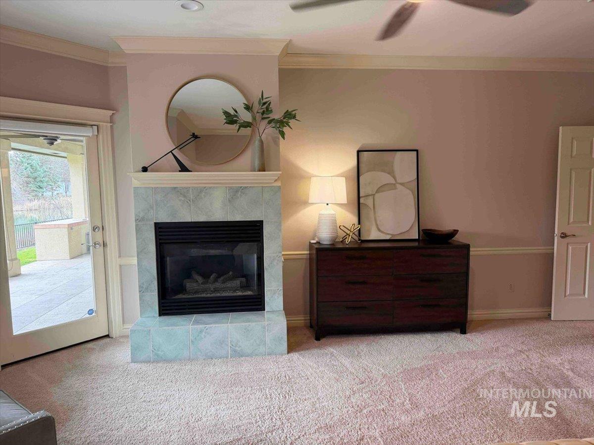 Detailed view of ornamental molding, a tiled fireplace, carpet floors, and a ceiling fan