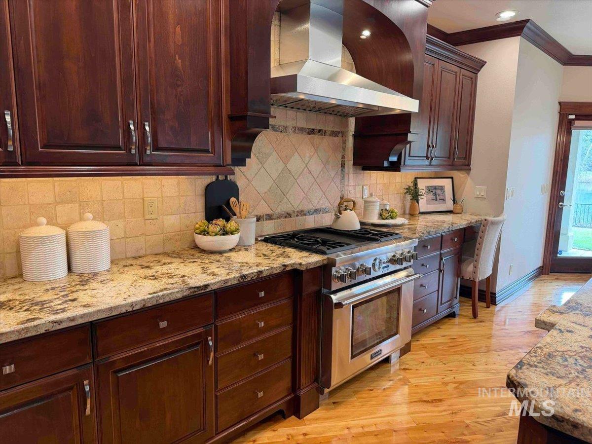 Kitchen with crown molding, light stone counters, stainless steel range, light wood-style flooring, and dark wood finish cabinets