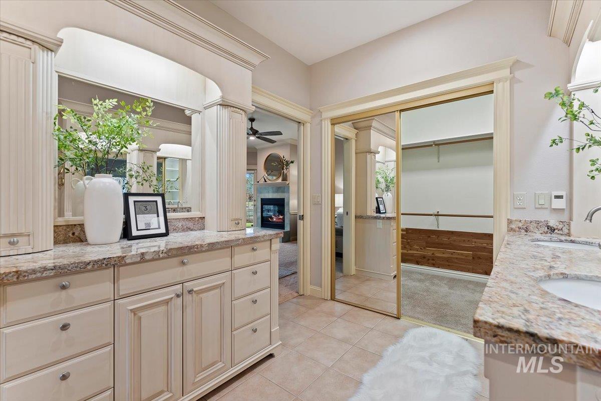 Bathroom featuring double vanity, a walk in closet, a glass covered fireplace, light tile patterned floors, and ornate columns