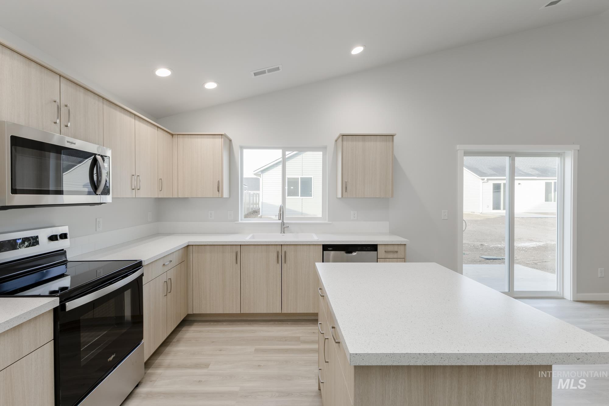 Kitchen featuring light brown cabinets, stainless steel appliances, lofted ceiling, light wood finished floors, and modern cabinets