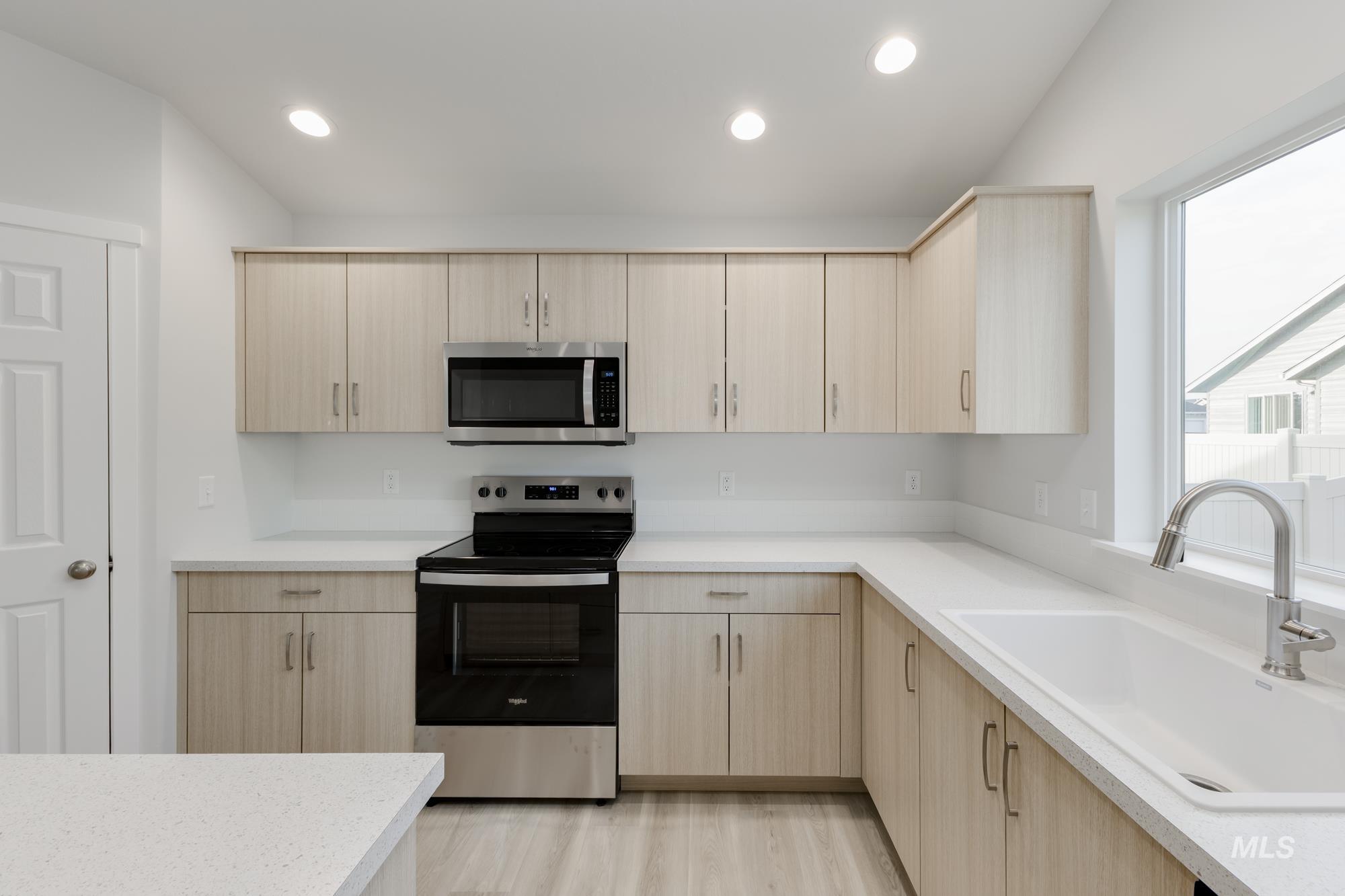 Kitchen featuring light brown cabinetry, appliances with stainless steel finishes, recessed lighting, light wood finished floors, and light stone countertops