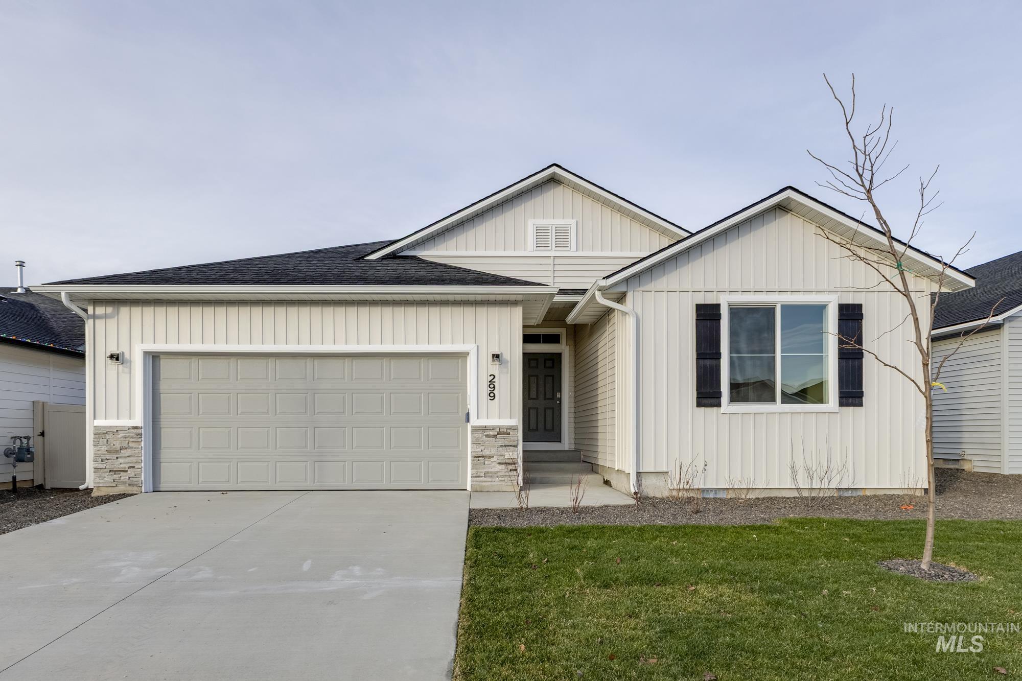 View of front of property featuring board and batten siding, driveway, an attached garage, a front lawn, and stone siding