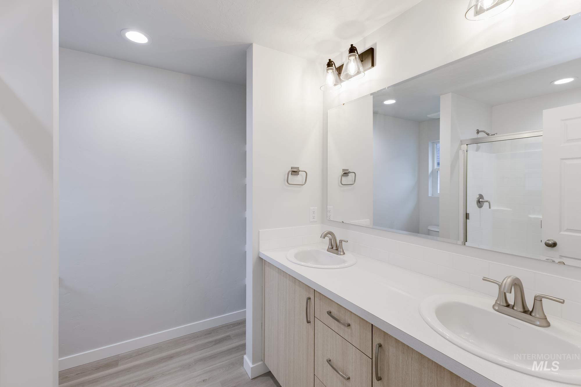 Full bathroom featuring double vanity, recessed lighting, a stall shower, and light wood finished floors