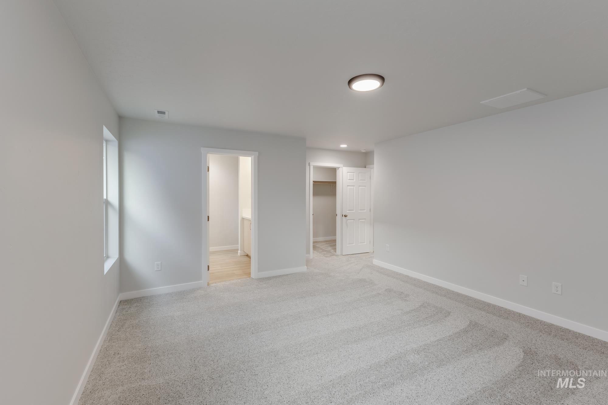 Unfurnished bedroom featuring a spacious closet, light carpet, and ensuite bathroom