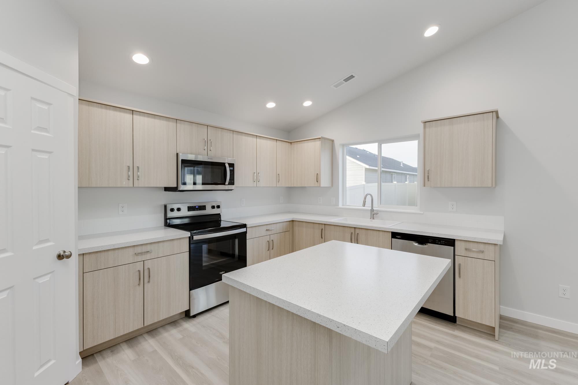 Kitchen featuring light brown cabinetry, stainless steel appliances, a center island, light wood-type flooring, and lofted ceiling