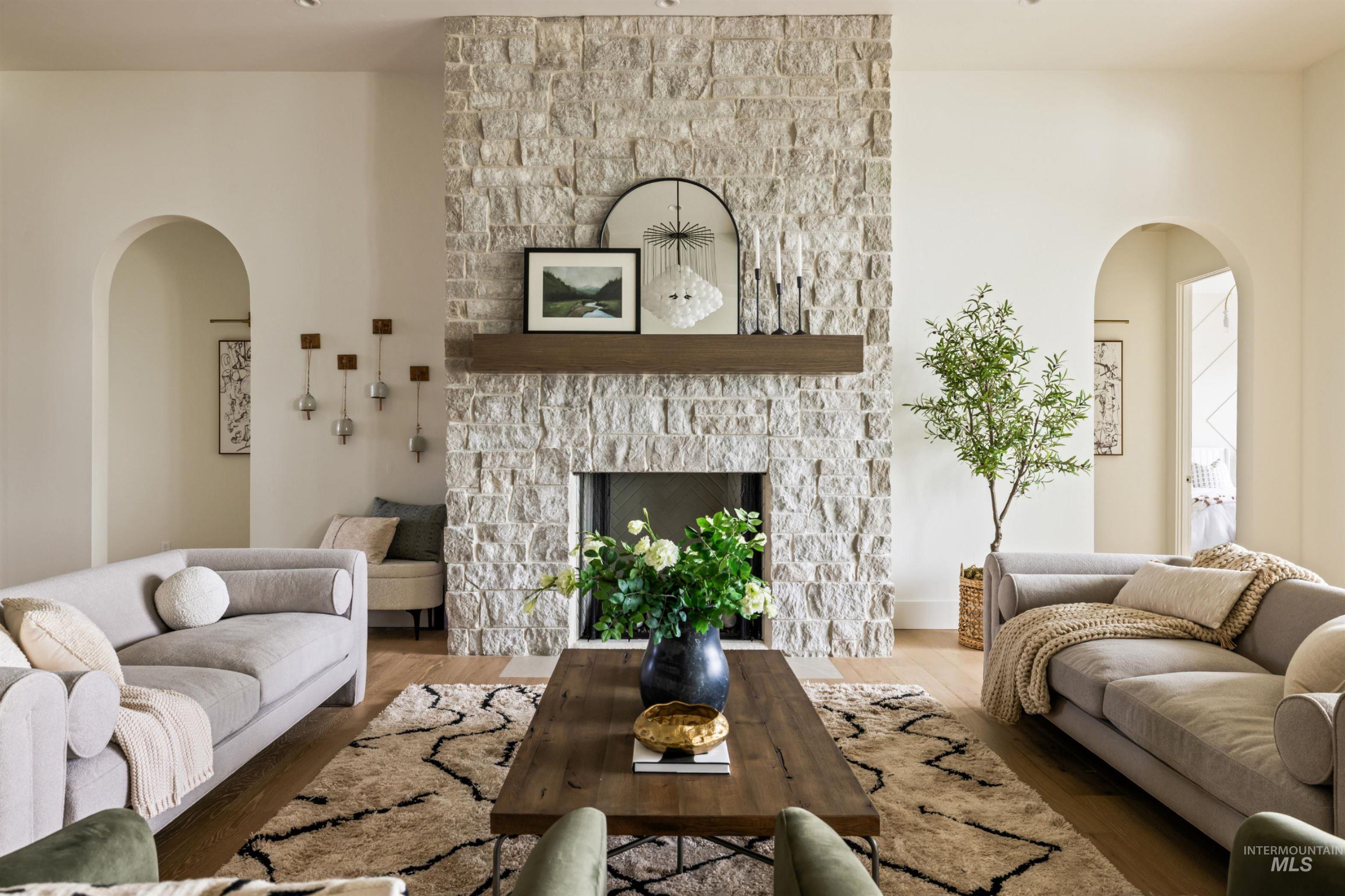 Living room with arched walkways, wood finished floors, and a stone fireplace