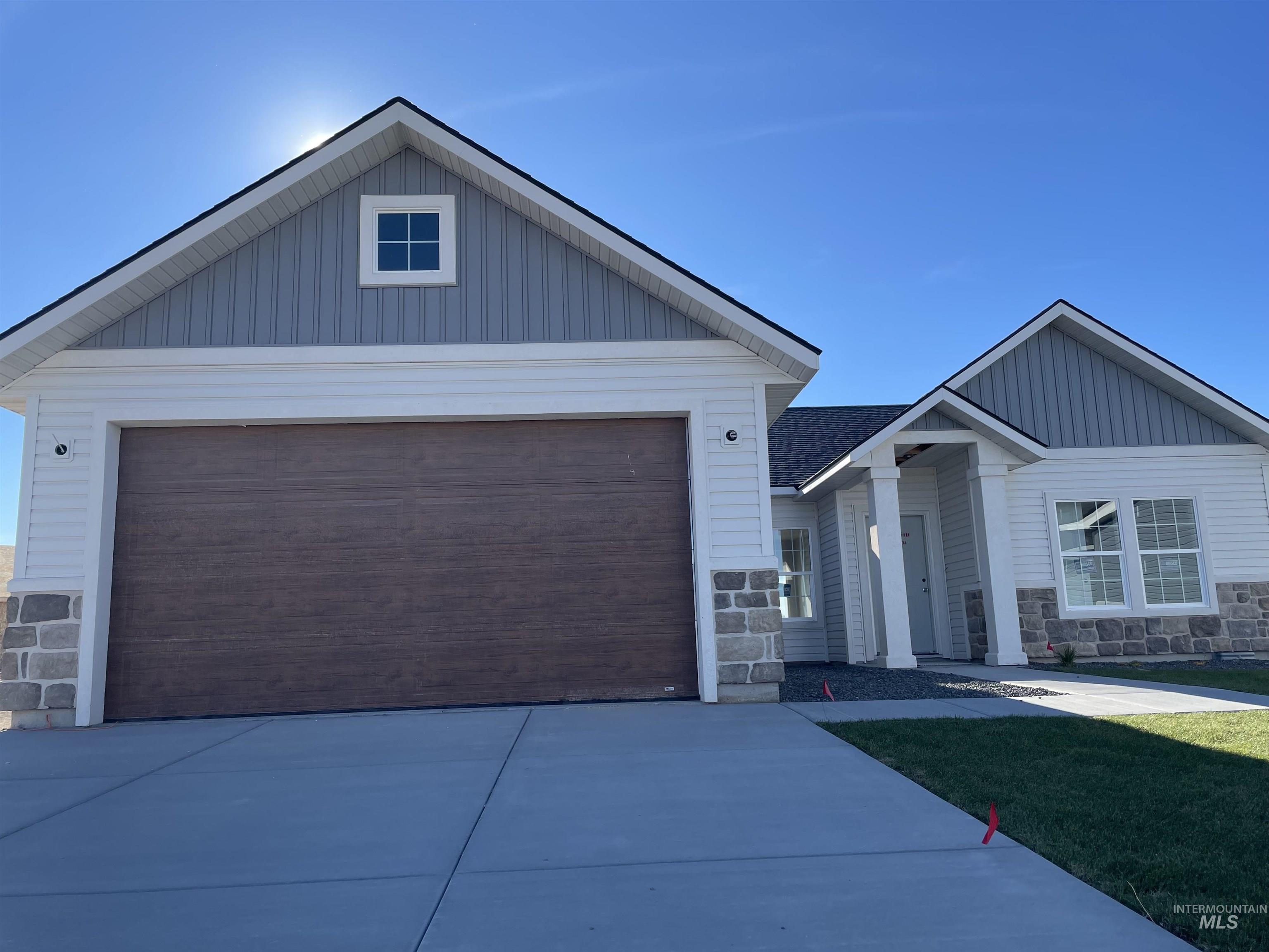 View of front of property with stone siding, a garage, board and batten siding, and driveway