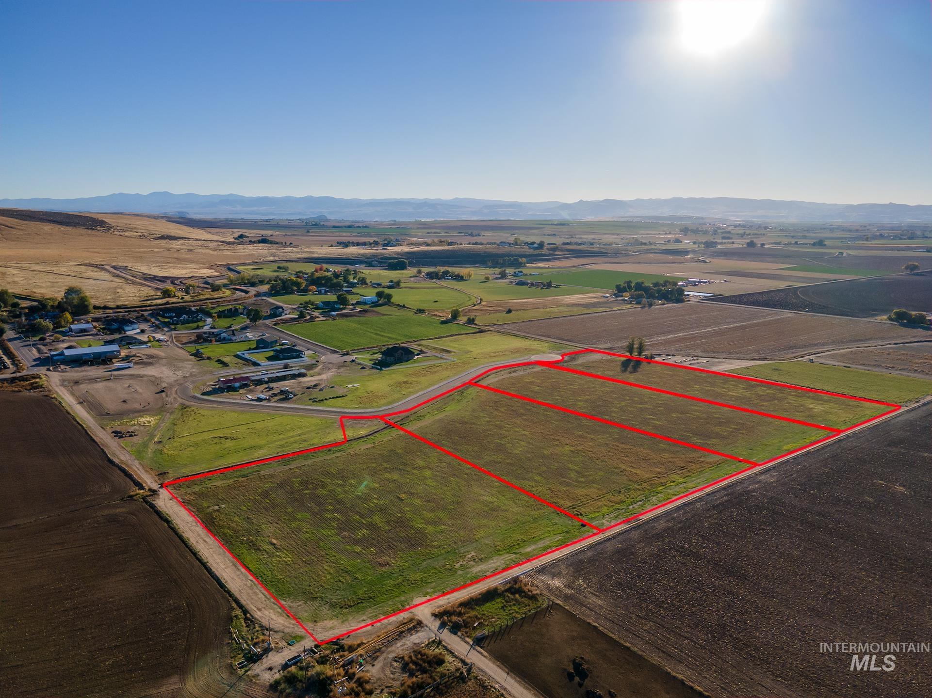 Aerial view of sparsely populated area featuring property boundaries highlighted, a mountain backdrop, and large plots for crops