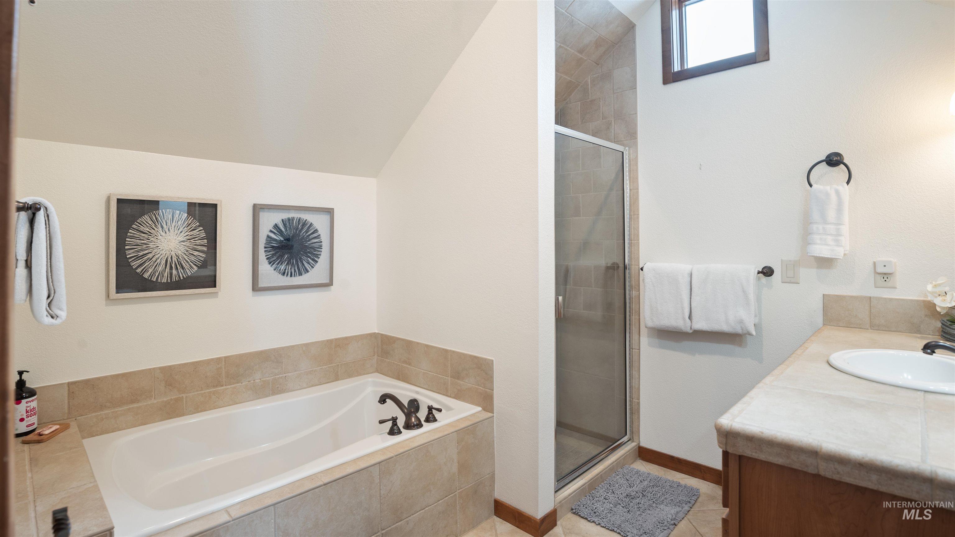 Full bathroom featuring lofted ceiling, vanity, a garden tub, a stall shower, and light tile patterned floors