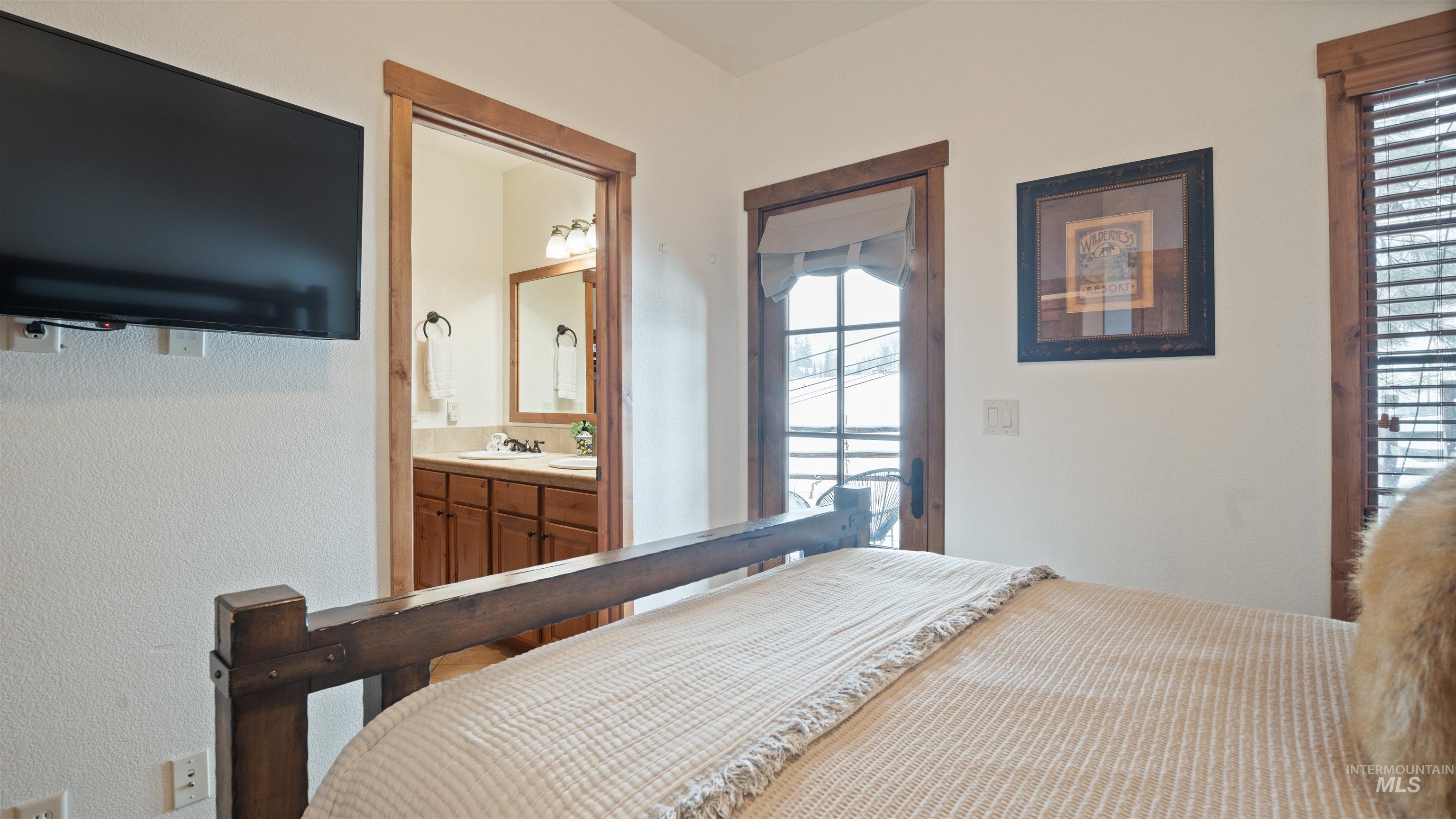 Bedroom with multiple windows, ensuite bathroom, access to exterior, and a textured wall