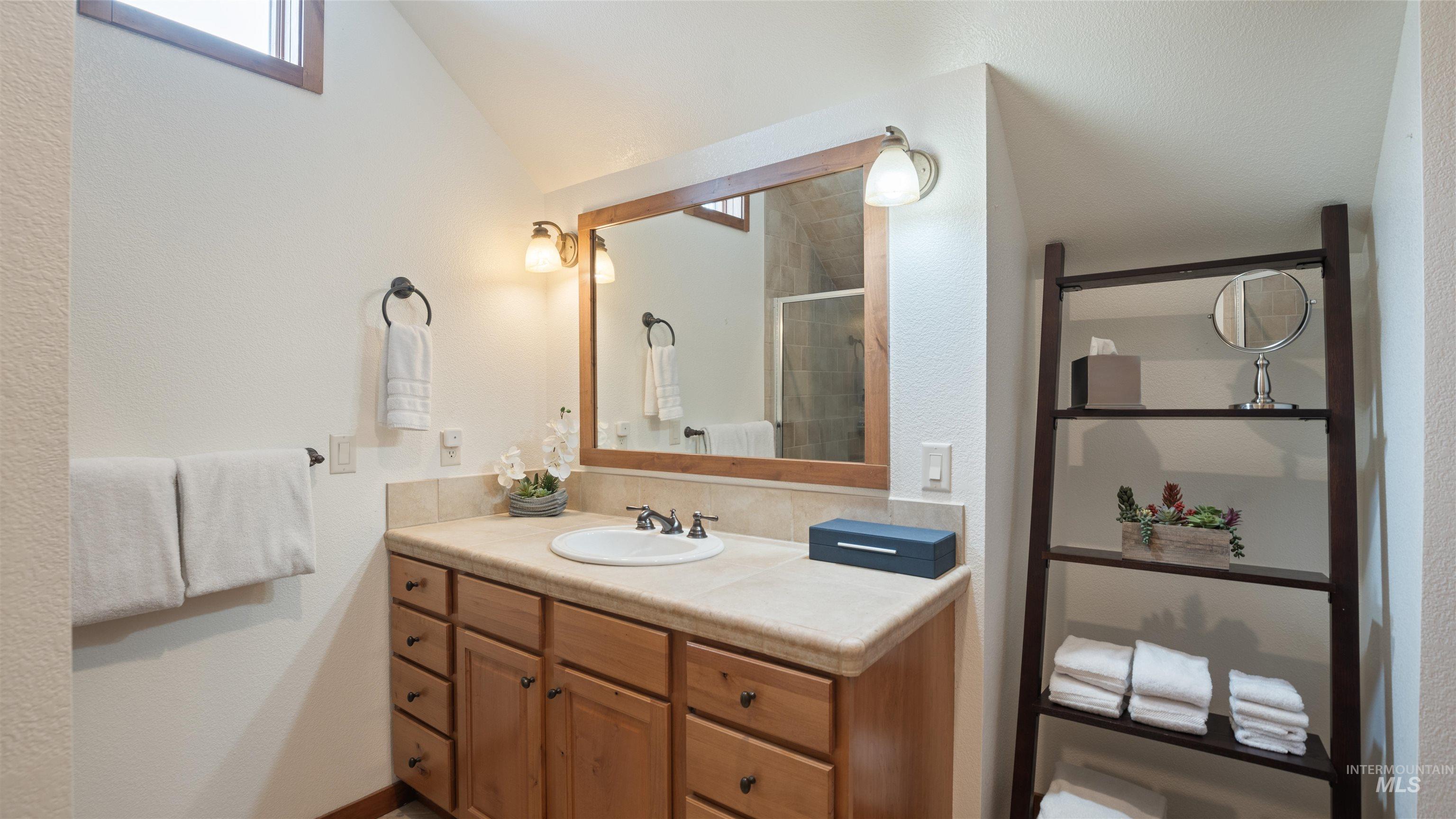 Full bathroom with vanity, a shower stall, a textured wall, and vaulted ceiling